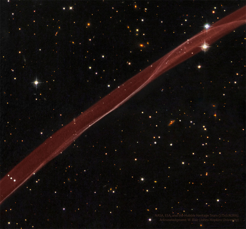 Debel prozoren trak rdečega plina poteka od spodaj leve do
zgoraj desne strani slike. Temno zvezdno polje z zvezdami in galaksijami obdaja
svetlo rdeč trak.
Za podrobnejše informacije si oglejte razlago.