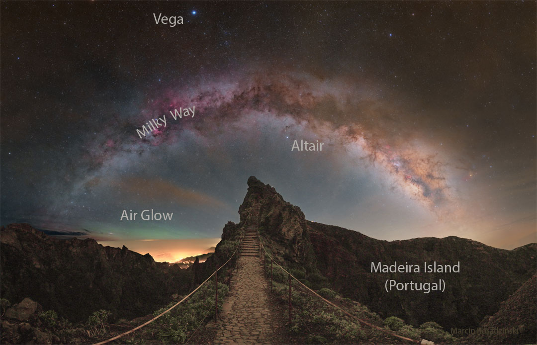 A star filled sky shows the arch of the central band of
our Milky Way galaxy across the top of the image. In the foreground
is a rocky landscape with a hill ahead and a pathway that leads
to stairs up that hill.
Please see the explanation for more detailed information.