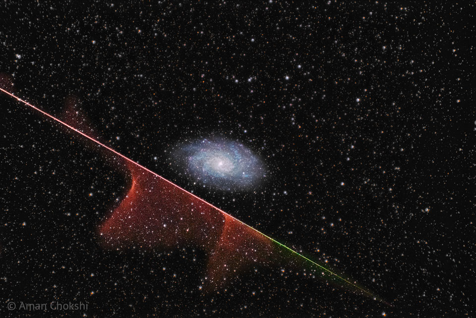 A distant spiral galaxy is seen in the image center.
A multi-colored streak runs diagonally across the image
from the upper left to the lower right. Parts of this
streak have gas near it. The background is dark field
filled with stars.
Please see the explanation for more detailed information.