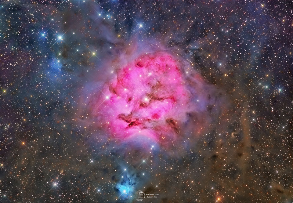 A red emission nebula is shown against a busy starfield
with many dark dust filaments near the nebula's center.
Near the bottom of the image is a smaller blue reflection
nebula.
Please see the explanation for more detailed information.