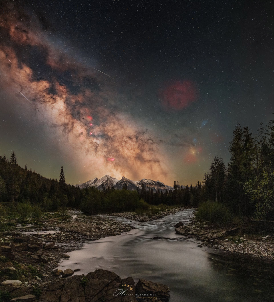 A starry sky is shown with the busy central band of
our Milky Way Galaxy showing diagonally from the upper left.
Mountains are on the horizon, with trees and a stream running
up from the foreground.
Please see the explanation for more detailed information.