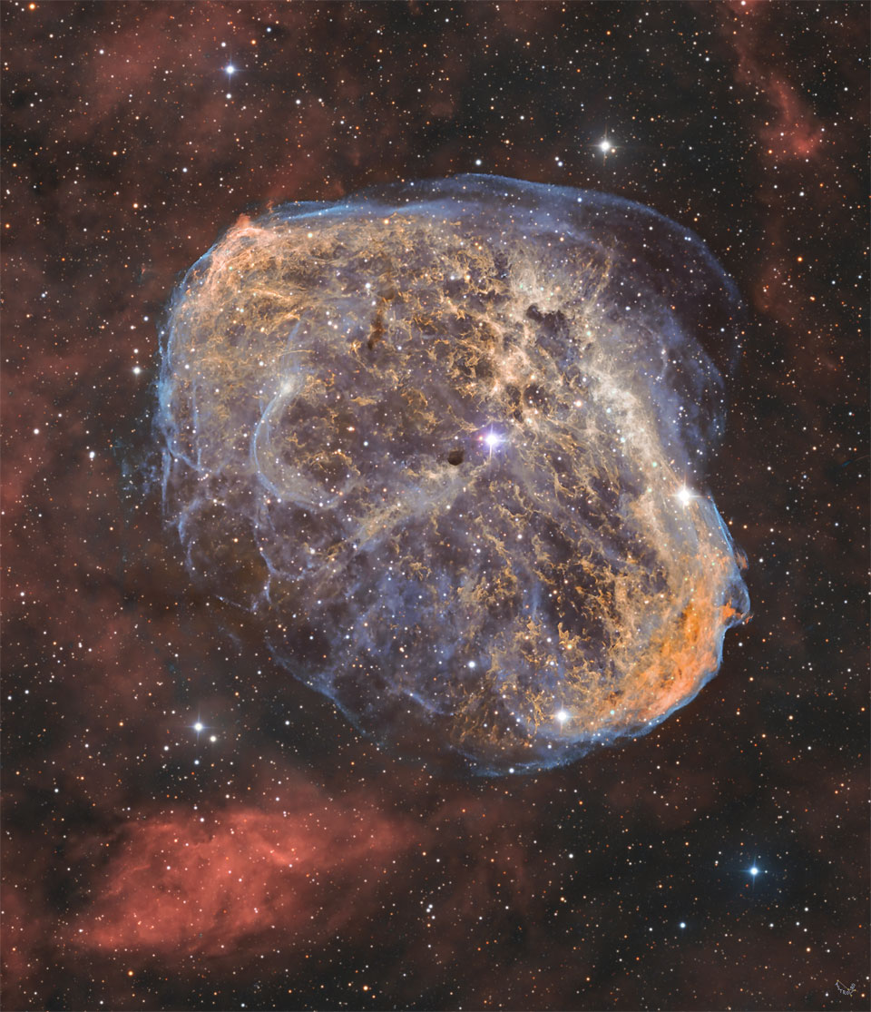 A starfield is shown with a unusual textured nebula
in the center colored in brown with blue trimmings. Diffuse
red nebula appear around the edges. In the center is an
opaque brown object.
Please see the explanation for more detailed information.