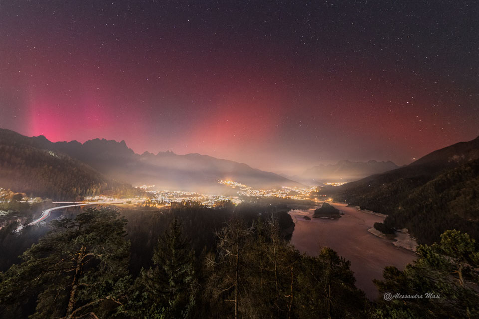 A star field appears above a town at night. The left part
of the sky shows a pinkish-red glow that is an aurora, while the
right part of the sky shows a smoother and darker glow that is
a SAR arc.
Please see the explanation for more detailed information.