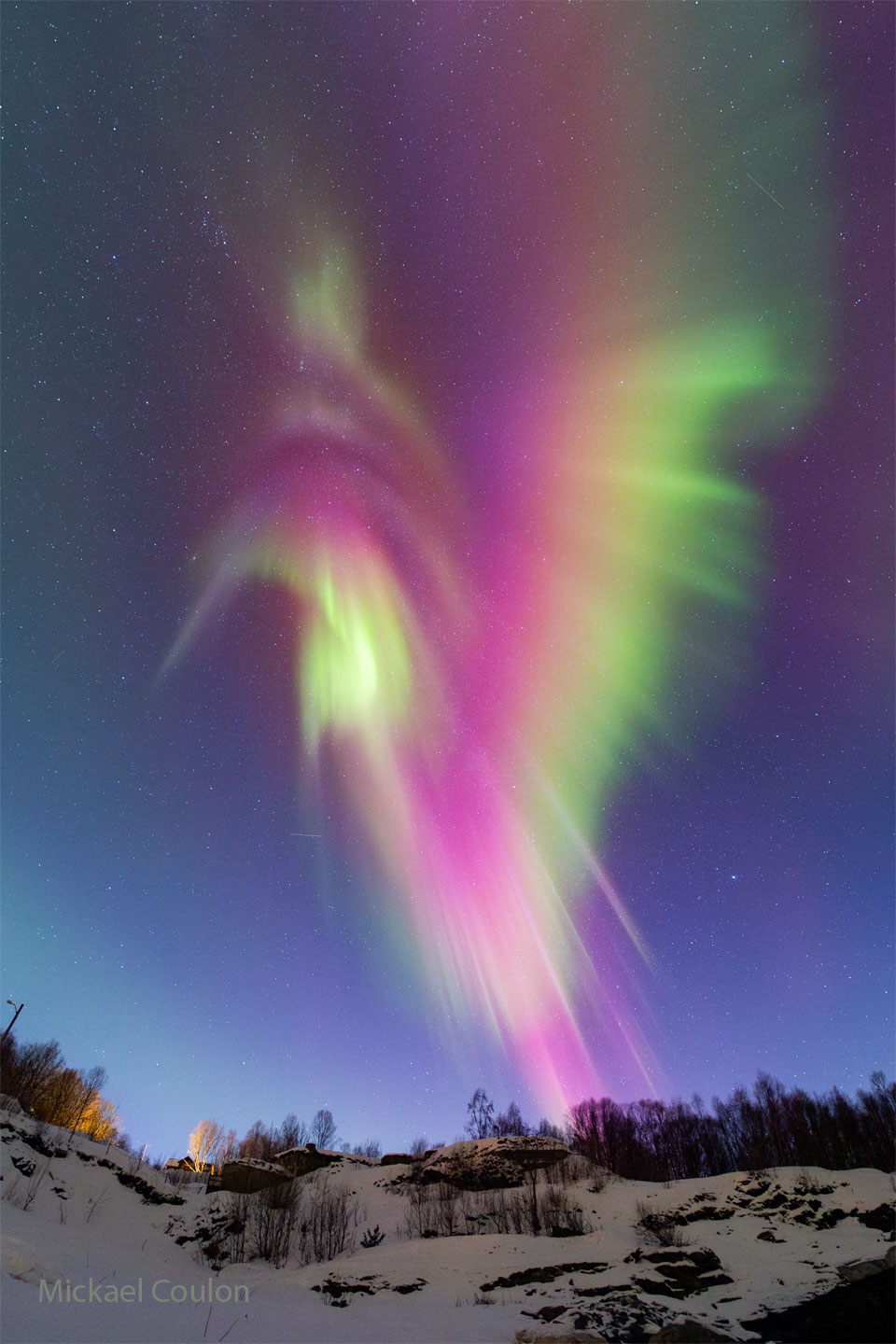 A snowy landscape sits below a star filled sky.
Dominating the frame is a large aurora in red, green,
yellow, purple, white.
Please see the explanation for more detailed information.