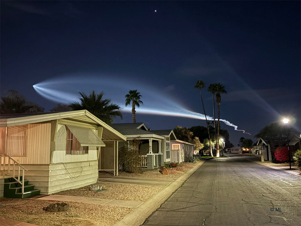 Houses are seen on a street below the night sky.
In the sky is a bright light plume that looks like the outline
of a giant fish.
Please see the explanation for more detailed information.