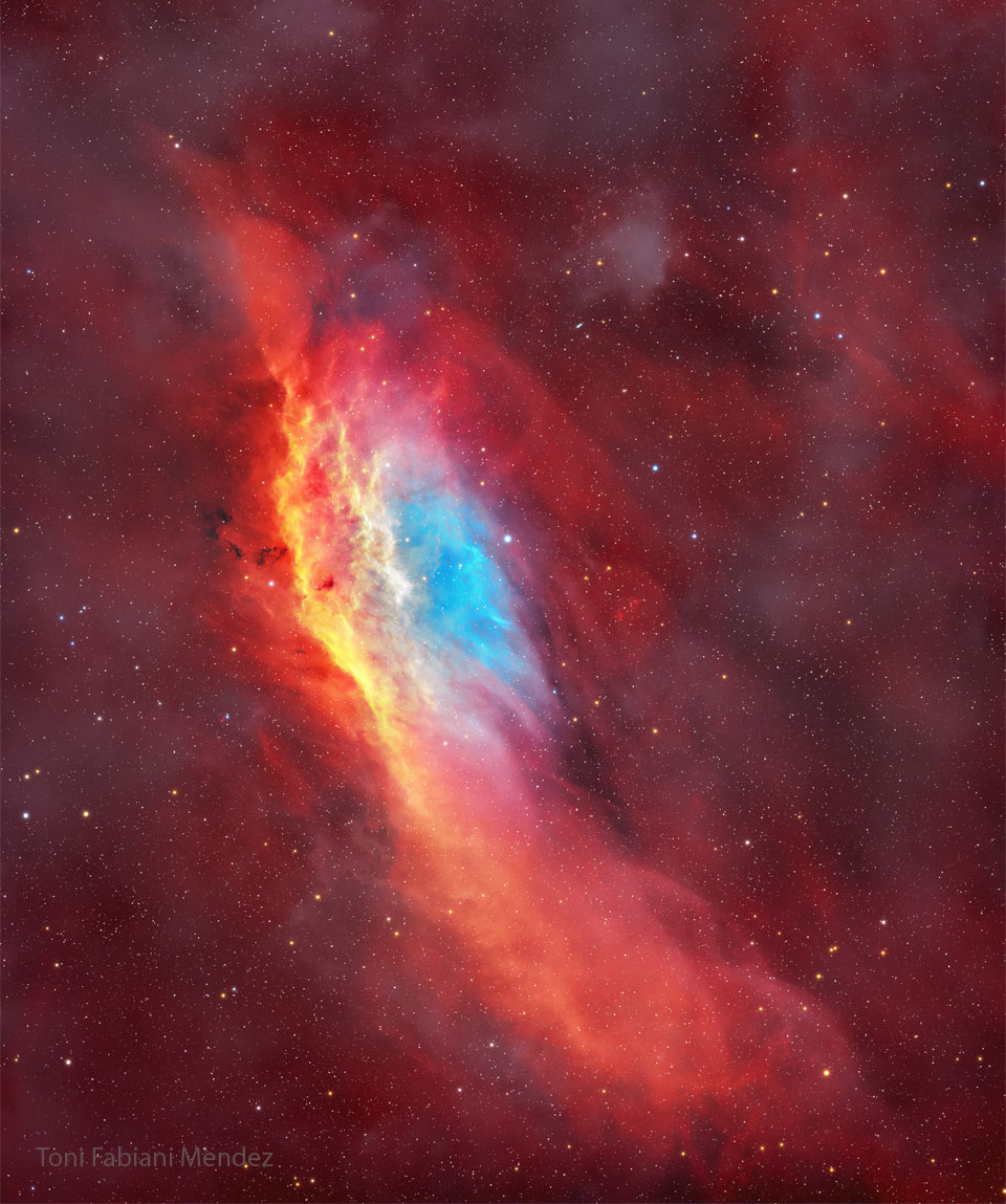 The starry image filled with a red glow features
a red, yellow, and blue colored nebula. The nebula
has, roughly, the shape of the US state of California.
Please see the explanation for more detailed information.