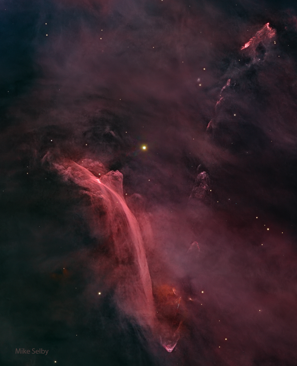 A starfield filled with a diffuse red glow has an
unusual nebula on the lower left. The nebula has bright
red filaments that curve down and appear to be reminiscent of
a waterfall on Earth.
Please see the explanation for more detailed information.