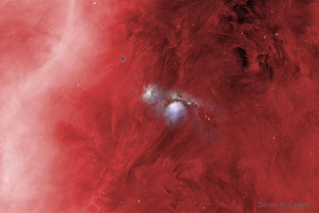 In a starfield glowing red, several features stand
out. On the right is a diffuse white band, and on the
upper right is some dark dust. Most prominently, though,
are two blue structures in the center, one of which has
a dark band running across near the middle.
Please see the explanation for more detailed information.