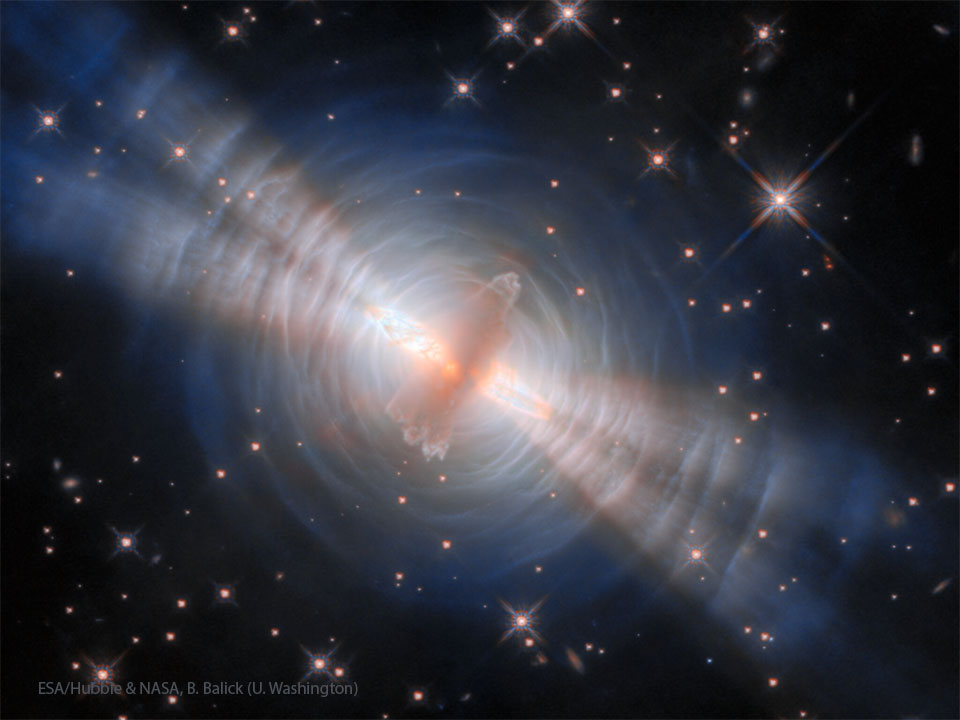 A starfield is shown with an unusual orange object in the center.
Surrounding this object are blue rings and four thick jets.
Please see the explanation for more detailed information.