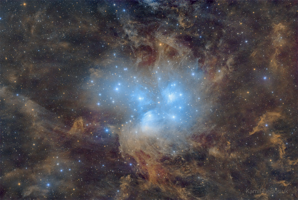 A cluster of blue stars is seen against a starfield
of brown and clumpy dust. The stars illuminate some of
the nearby dust which causes the dust to glow blue.
Please see the explanation for more detailed information.
