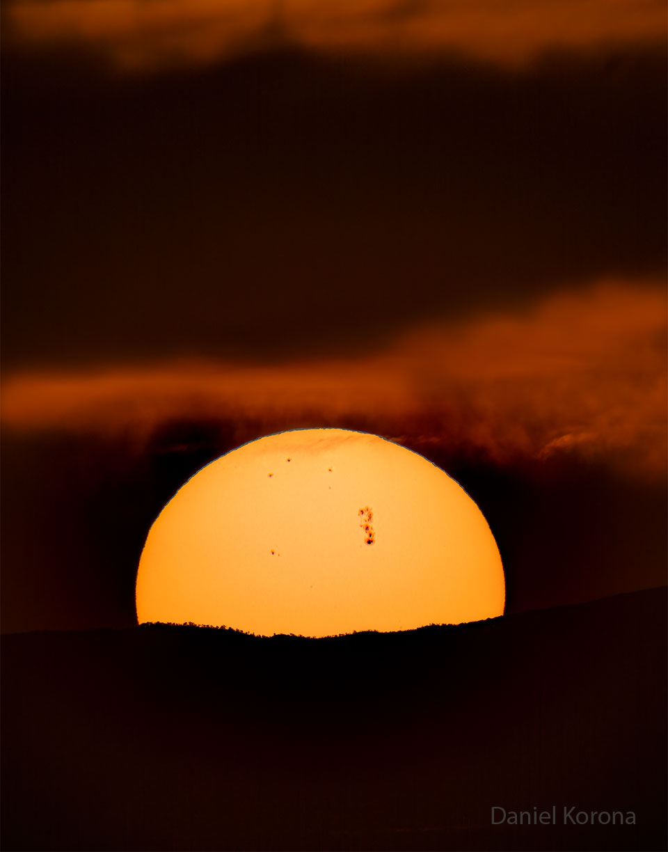 Most of the Sun is pictured peeking over a hill.
On the surface of the Sun are several sunspots including
a very large sunspot region toward the center-right.
Please see the explanation for more detailed information.