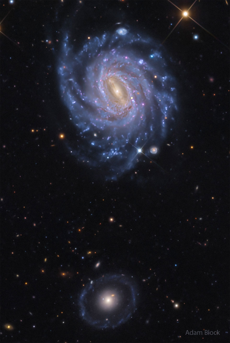 A starfield is shown showing two prominent galaxies.
Near the top is a bright spiral galaxy with several blue
spiral arms. Near the bottom is a fainter circular
galaxy with a bright center.
Please see the explanation for more detailed information.