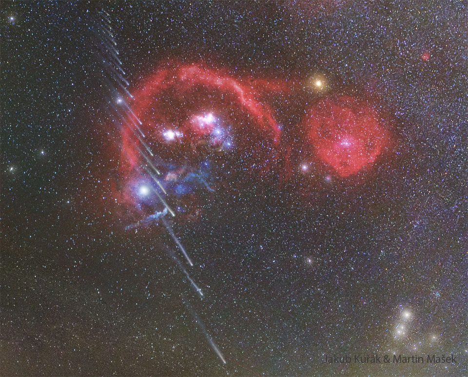 A starfield shows many red nebulas near the center.
Running vertically up the left side are about 20 images of a
comet, with the head towards the image bottom.  Successively
higher images of the comet show successively shorter
tails.
Please see the explanation for more detailed information.