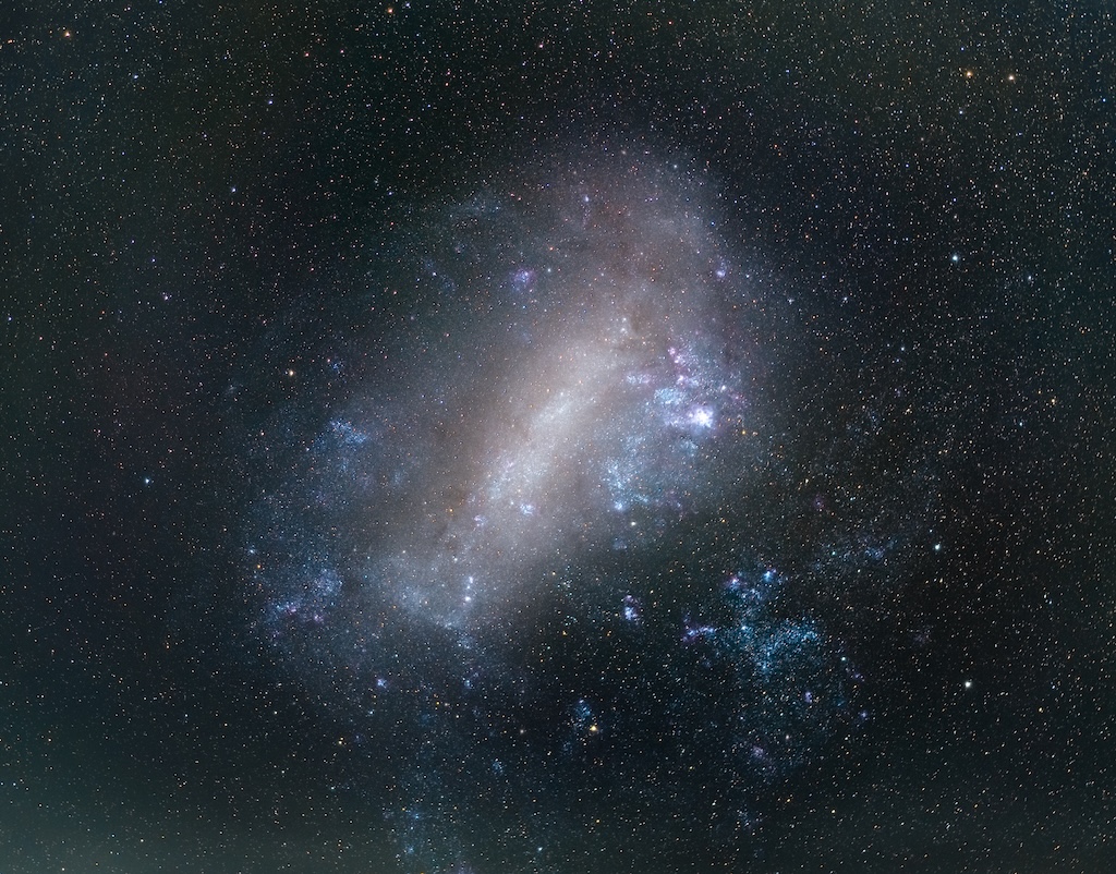 A galaxy with stars and colorful clous of gas.
	  The background is a dark field of stars. 