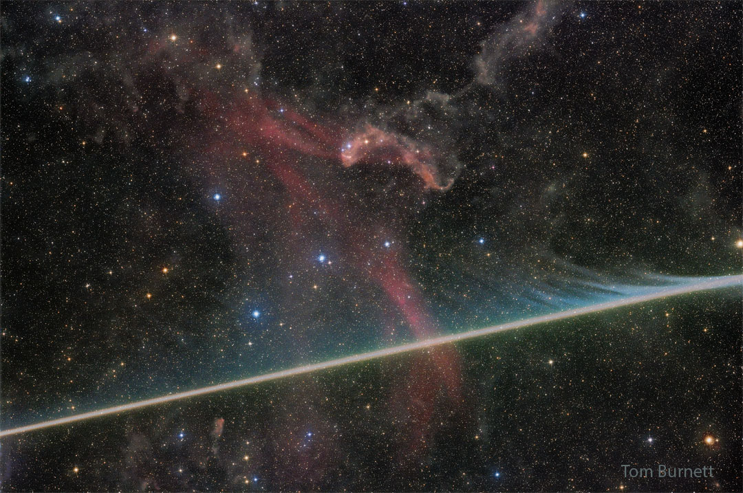 A dark starfield has a faint red nebula near
the center. A bright streak crosses the image
horizontally from the lower left, filled with faint
evaporating wisps in many colors.
Please see the explanation for more detailed information.