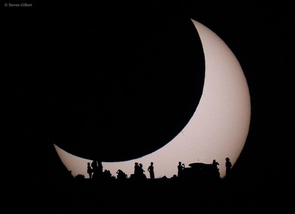 A light disk is visible on the lower left but the
rest of the disk is eclipsed by a darker disk of the
same apparent size. At the bottom of the image are the
silhouettes of several people.
Please see the explanation for more detailed information.