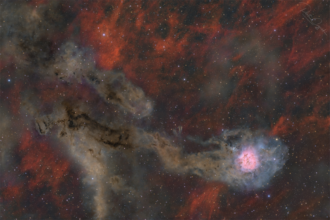 A starfield is shown against a patchy red-glowing
background. Two irregular brown trails occur, the lower
of which culminates in a bright pink and white region.
Please see the explanation for more detailed information.